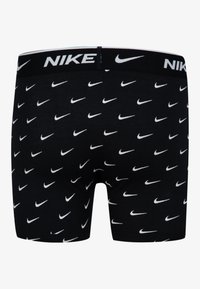 Melnas bokseršortas ar baltām Nike logotipiem atkārtotā rakstā. Iezīmēts ar melnu elastīgu jostu, kurā baltā krāsā ir rakstīts "NIKE". Mīksts kokvilnas materiāls.