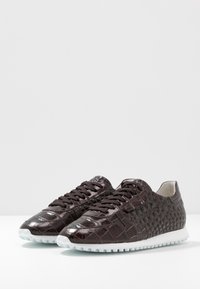 Baskets marron foncé avec un motif crocodile texturé, bout rond et semelles en caoutchouc blanc. Elles disposent de lacets marron et d'un design bas.