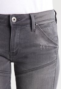 Šedé džíny z denimu s přiléhavým střihem, jemným opotřebením, předním zapínáním na knoflík a pěti kapsami. Texturovaný povrch s mírným leskem.