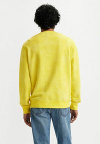 Gele sweatshirts, zachte katoenmateriaal, ronde hals, lange mouwen, met een tie-dye patroon. Gepaard met lichtblauwe denim jeans.