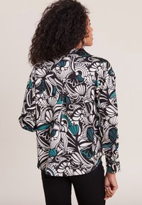 Langsleeve shirt met een zwarte achtergrond en een gedurfde witte en teal bloemenpatroon. Materiaal lijkt lichtgewicht met een relaxte pasvorm.