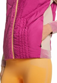 Fuchsia Steppweste mit strukturierter Polsterung und Reißverschluss, kombiniert mit enganliegenden gelben Leggings mit Netzmuster und soliden Akzenten.