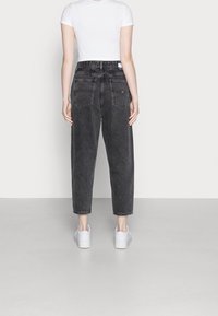 Černé džíny s vysokým pasem a rovnými nohavicemi, s dvěma zadními kapsami a ohrnutými lemy, zkombinované s bílými teniskami.