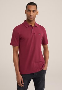 Bordo polo marškiniai su klasikine apykakle ir dviem mygtukais. Yra išsiuvinėtas logotipas ant krūtinės ir trumpomis rankovėmis.