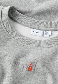 Lichtgrijze sweatshirt-halslijn met de tekst "Gris pâle" in verhoogde letters, waarbij de letter "â" in het rood is, en het maatlabel toont 7-8 jaar.
