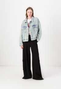 Light blue denim jacket with two chest pockets and a relaxed fit, paired with black wide-leg trousers featuring cargo pockets.