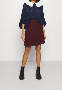 Pull en tricot bleu marine avec un col blanc, associé à une jupe évasée bordeaux et des bottines noires à lacets.
