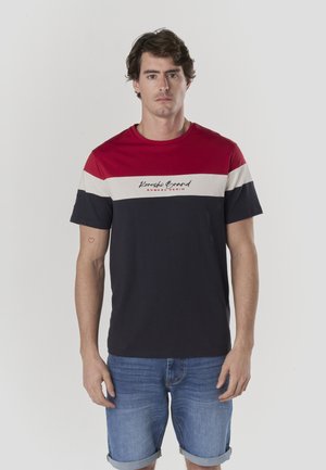 Camiseta de manga corta con franjas horizontales en rojo, blanco y azul marino, de algodón, con texto de logotipo en el frente. Combinada con shorts vaqueros.