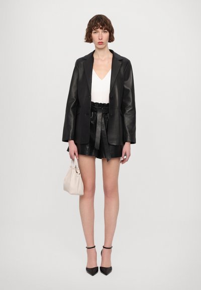 Black leather blazer paired with a white V-neck top and black leather shorts. Accessories include a beige bag and black heeled shoes.