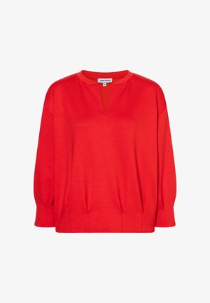 Blouse rouge à manches longues avec un décolleté en V, col rond et légers plis près de l'ourlet.