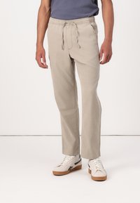 Pantalon en coton beige avec une taille élastique, fermeture par cordon de serrage et coupe droite ; associé à des baskets légères.