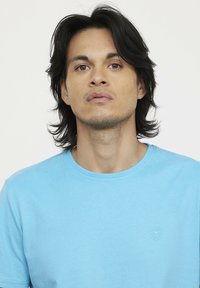 Hellblaues Baumwoll-T-Shirt mit rundem Ausschnitt und kurzen Ärmeln. Es hat ein kleines strukturiertes Logo im linken Brustbereich.