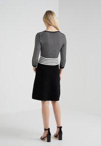 Robe à rayures noires et blanches avec manches trois-quarts et corsage ajusté, évasée en une jupe noire longueur genou ; matière texturée.