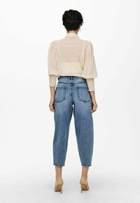 Przezroczysta beżowa bluzka w kropki, z bufkami, w zestawie z jasnoniebieskimi spodniami o wysokim stanie i cielistymi szpilkami.