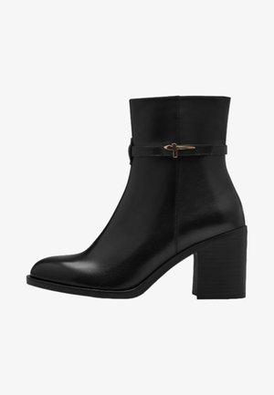 Black leather ankle boots with a tapered toe, medium block heel, and decorative strap featuring a gold accent. Smooth texture and sleek design.