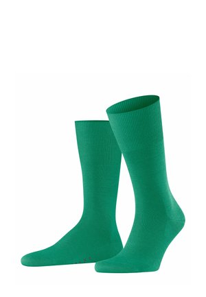 Deux chaussettes vertes présentées debout, avec un poignet côtelé et un corps lisse, mettant en valeur leur couleur vibrante et leur design.