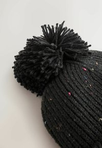 Mustra musta kootud beanie, millel on tekstuuriga ribakiri ja suur karvane pom-pom peal, mis on kaunistatud värviliste täppidega kogu kangas.