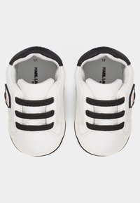 Λευκά βρεφικά παπούτσια με μαύρα κορδόνια και επένδυση, μαλακές σόλες και ένα μικρό κυκλικό σήμα στο πλάι, απόψη κορυφής.