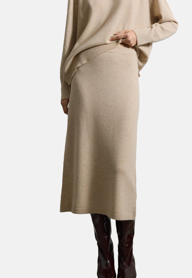 Suéter de punto beige y falda midi a juego con detalles acanalados. El modelo lleva botas burdeos hasta la rodilla. Textura suave, corte relajado.