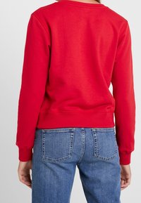Felpa rossa in cotone con girocollo e polsini a costine, abbinata a jeans in denim blu con tasche posteriori e design a gamba dritta.