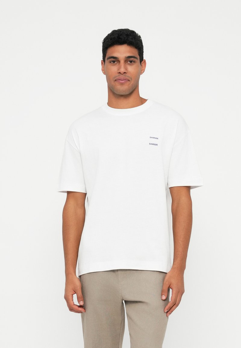 White cotton t-shirt with short sleeves, featuring a small black "Samsøe" logo on the chest. Casual fit with a round neckline.