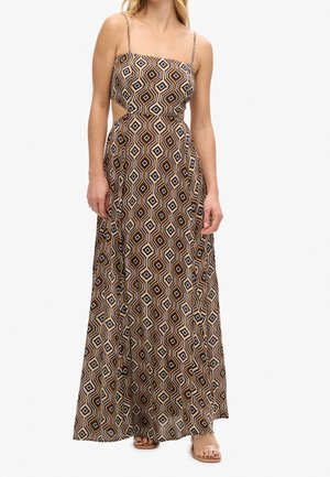 Femme portant une robe sans manches, longue, avec un motif géométrique en losanges marron, noir et beige, et des découpes à la taille.