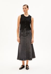 Gilet sans manches noir avec un col en V et des boutons sur le devant, associé à une jupe en denim noir longue et évasée présentant des détails de couture visibles.