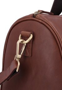 Sac en cuir marron avec quincaillerie dorée, présentant une forme arrondie et un attachement à clip. Surface texturée avec des détails de couture visibles.