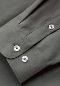 Gros plan sur un poignet de chemise grise avec deux boutons blancs transparents et des coutures visibles sur un tissu doux.