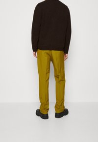 Brązowy sweter dzianinowy w połączeniu z musztardowymi spodniami i czarnymi butami. Strój charakteryzuje się luźnym krojem i teksturowanym wykończeniem.