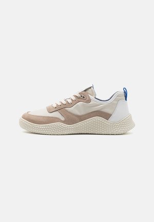 Baskets avec une tige beige et marron clair, en matériaux en daim et synthétiques, semelle blanche texturée, structure semi-rigide et accents bleus.