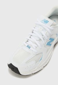 Adidași albi pentru alergare cu accente albastre, plasă superioară și talpă texturată. Caracteristicile includ șireturi tradiționale și un guler căptușit pentru confort.