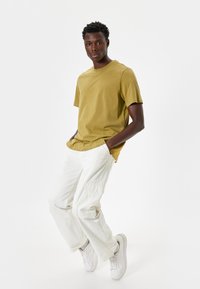 Olivengrøn kortærmet t-shirt parret med hvide cargo-bukser. Sneakersene er hvide. Enkel design med en afslappet pasform og minimale detaljer.