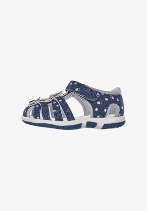 Sandal de denim azul con lunares blancos, correas anchas y cierre de gancho y bucle. Suela de goma para agarre y durabilidad.