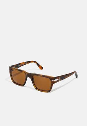 Schildpatt-Sonnenbrille mit rechteckigen Rahmen, braunen Gläsern und Metallakzenten an den Bügeln. Mattes Finish und gewagtes Design.