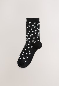 Chaussette basse noire avec des motifs de cœurs blancs partout. Texture douce, longueur standard, talon et pointe renforcés pour une meilleure durabilité.