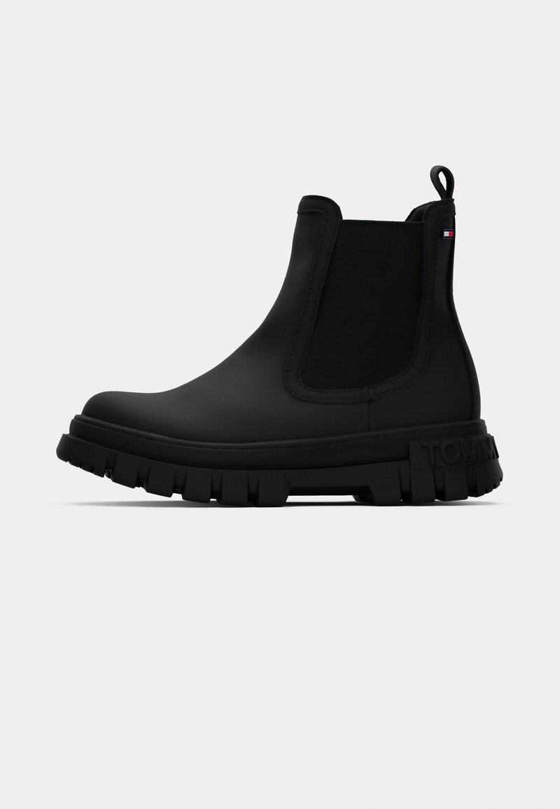 Fekete gumibakancs, textúrált elasztikus panellel, vastag barázdált talppal és húzófüllel a könnyű felhelyezéshez, a "TOMMY" felirattal.