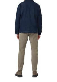 Jeansjacke in Dunkelblau, mit einem kragenförmigen Ausschnitt und Knopfverschlüssen, kombiniert mit beigen Hosen und braunen Wildlederschuhen.