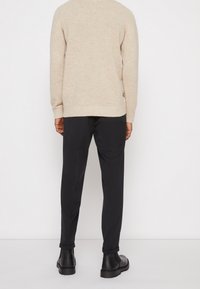 Beżowy sweter z dzianiny, luźny krój, prążkowane mankiety, zestawiony z czarnymi spodniami slim-fit, długości do kostek, oraz czarnymi skórzanymi butami na grubej podeszwie.