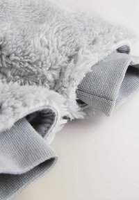 Jasnoszara tkanina polarowa o puszystej teksturze, z prążkowanymi szarymi rękawami. Projekt jest miękki, z mieszanką materiałów dla komfortu.