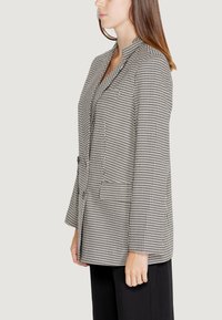 Blazer houndstooth bianco e nero con colletto a ribattuta, maniche lunghe e due tasche frontali, caratterizzato da una vestibilità su misura e una texture liscia.