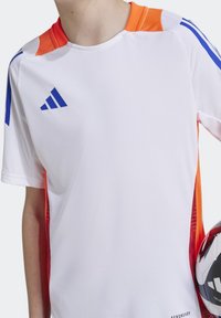 Camiseta deportiva blanca con acentos naranjas, franjas azules en los hombros y paneles laterales transpirables. Presenta el logo de adidas.