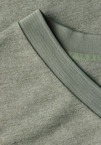 Oliwkowa, teksturowana dzianina z dekoltem w serek. Charakteryzuje się prążkowanym kołnierzem oraz subtelnymi, gładkimi odcieniami kolorów rozproszonymi w całej tkaninie.