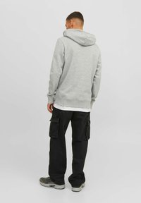 Sudadera gris con capucha, puños y cintura ajustados; combinada con pantalones cargo negros con bolsillos laterales. Modelo visto desde atrás.