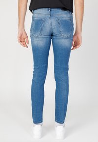 Vaqueros ajustados en denim de color azul claro, con un diseño desgastado, bolsillos traseros con costuras decorativas y un corte slim que se ajusta hasta los tobillos.