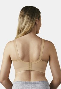 Beżowy biustonosz z szerokimi, regulowanymi ramiączkami i gładką fakturą. Posiada zapięcie na haftkę z tyłu. Uzupełniony szarym strojem do relaksu.