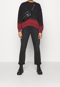 Felpa con gradiente nero e rosso, vestibilità comoda, abbinata a jeans neri a gamba dritta e stivali neri con lacci spessi; piccolo borsa a tracolla nera.