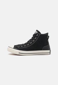Zapatillas altas negras de lona, con ojales de metal, puntera de goma blanca y costuras blancas en contraste. Etiqueta de la marca sutilmente visible.