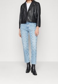 Svart läderk cropped bikerjacka med silverdetaljer, tillsammans med ljusblå jeans med metalliska prickar och svarta ankelboots.