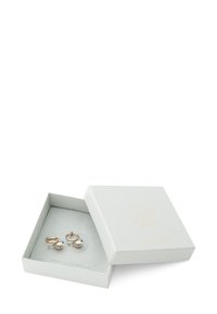 Guldtonede øreringe med en buet form og en perlefunktion. Pakkeret i en lys grå æske med struktureret overflade og præget logo.